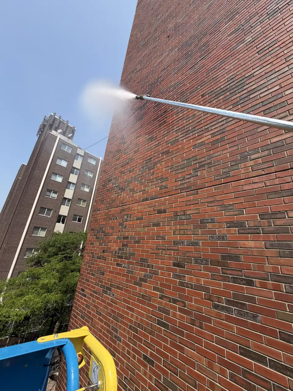 A long-range pressure washing nozzle cleaning a tall brick commercial building