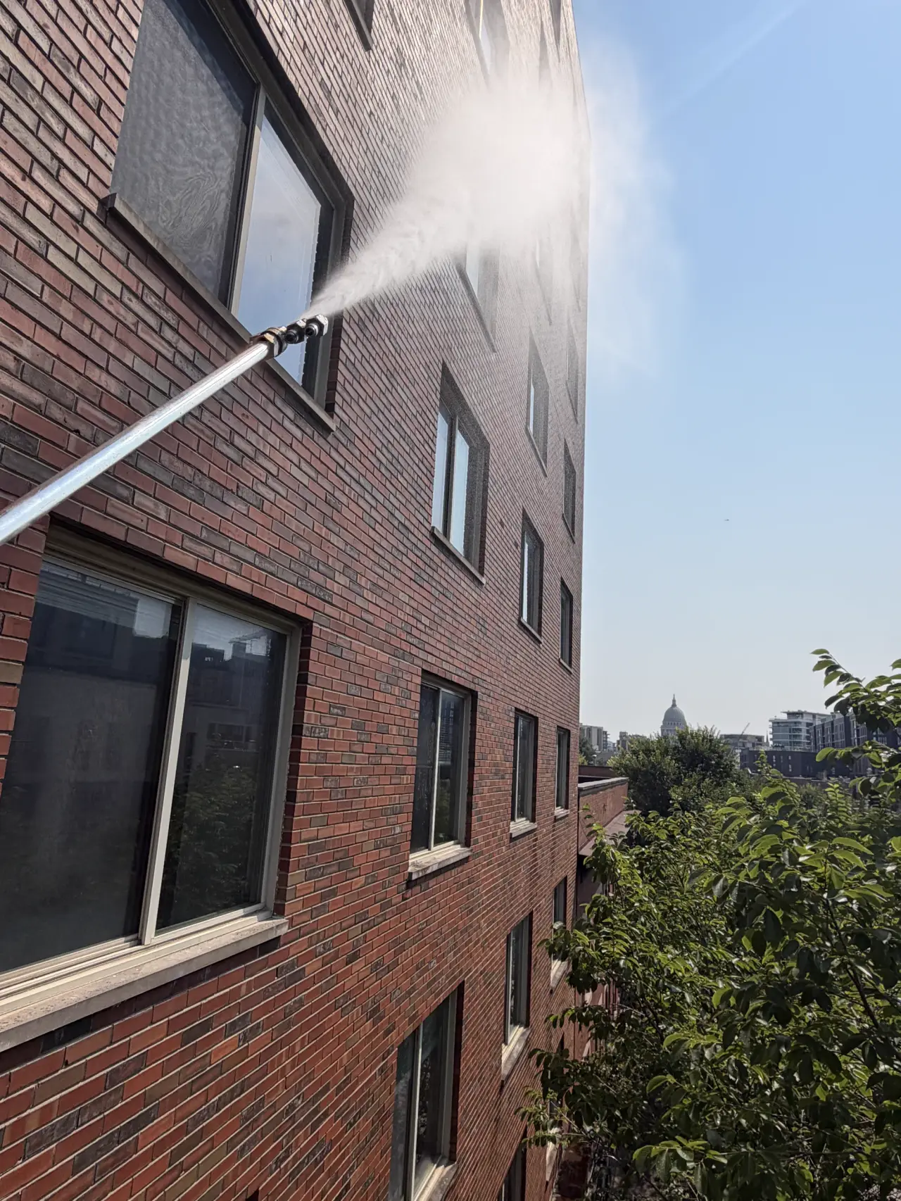 A water-fed pole rinsing an upper-floor window of a red-brick building with pure water — Madison, WI