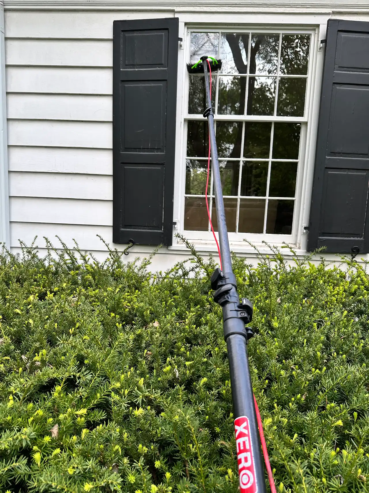 A XERO carbon-fiber water-fed pole cleaning a second-floor window on a white clapboard house — Madison, WI