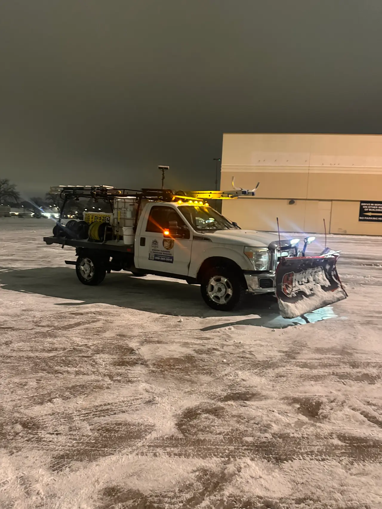 A Total Wash Co. plow truck with amber lights on in a snow-covered lot at night — Madison, WI