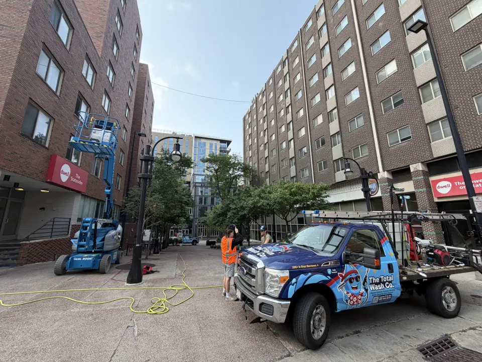 A Total Wash Co. truck and boom lift parked in front of large brick apartment buildings